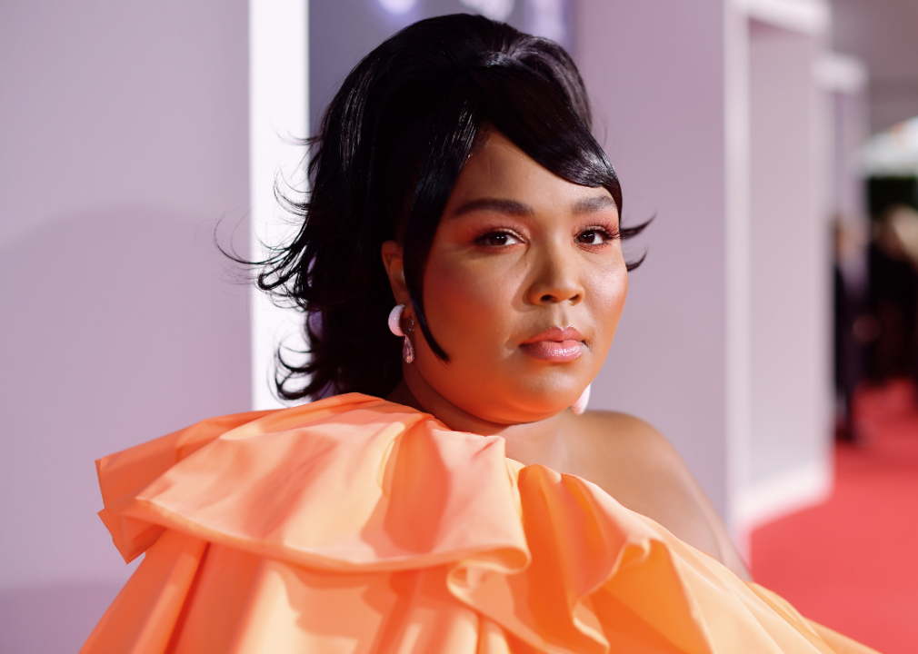 Lizzo wearing bright orange ensemble on red carpet.