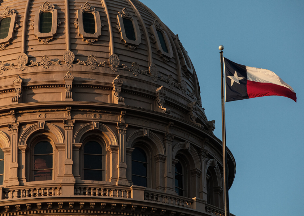 A Texas flag is displayed in front of the State Capitol building