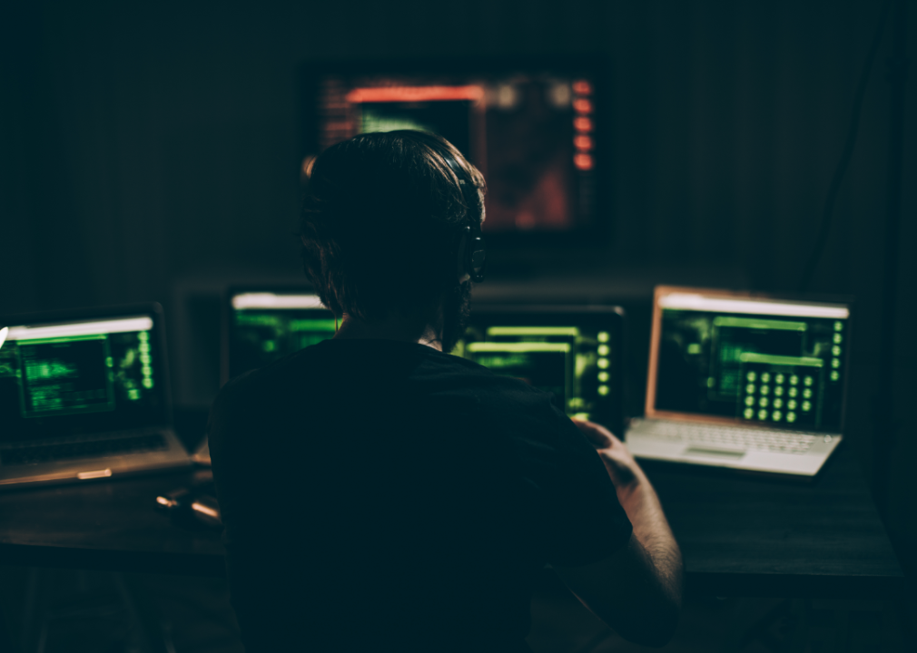 A coder sits in a darkened room looking at several screens