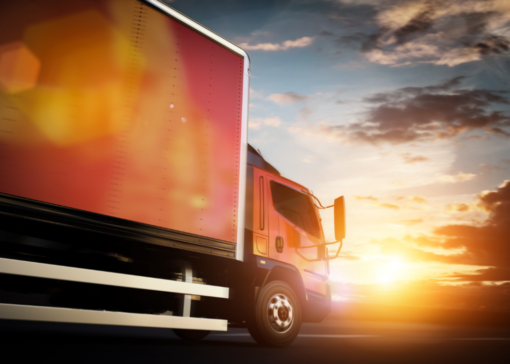 A moving truck speeds along a highway at sunset
