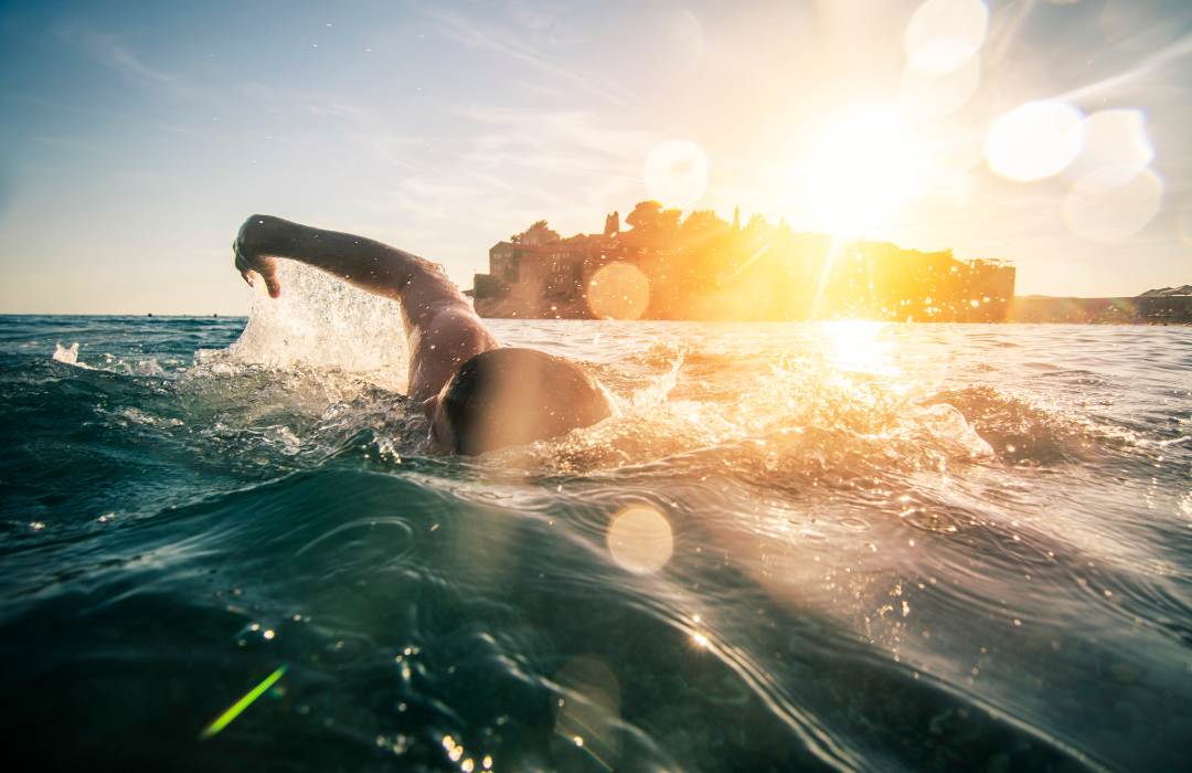 A man swimming in open water at sunset
