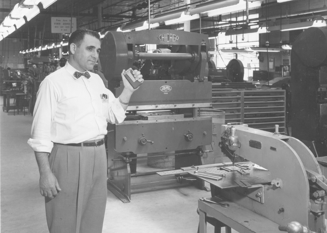 A man holding a pager on a factory floor in the 1950s
