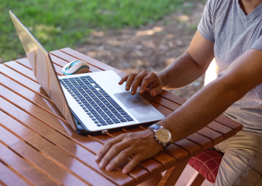 A man reads from his laptop at an outdoor table.