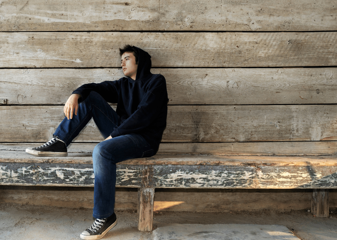 Young man in black hooded sweater sitting alone on bench