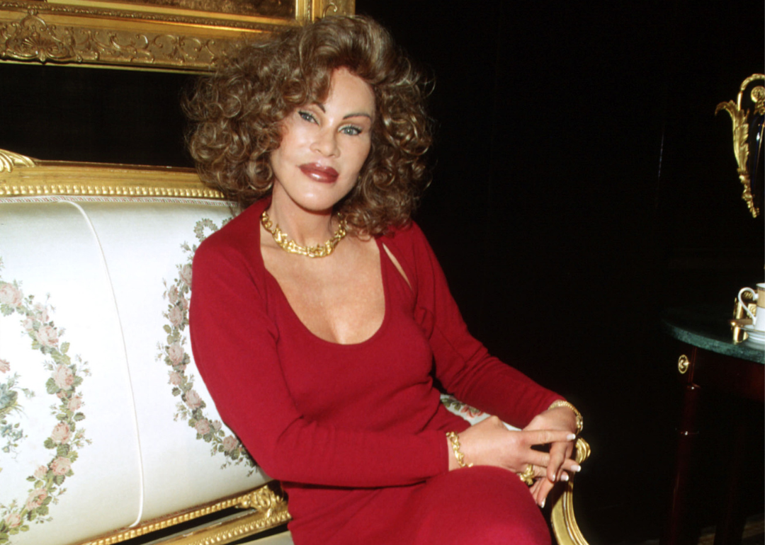 Jocelyn Wildenstein poses on an elaborate couch in front of a painting in a gilded frame.