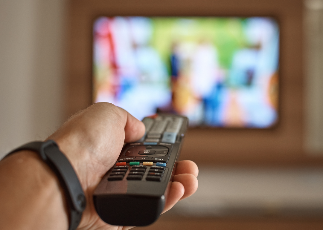 A hand holds a remote control as an ad plays on a TV screen