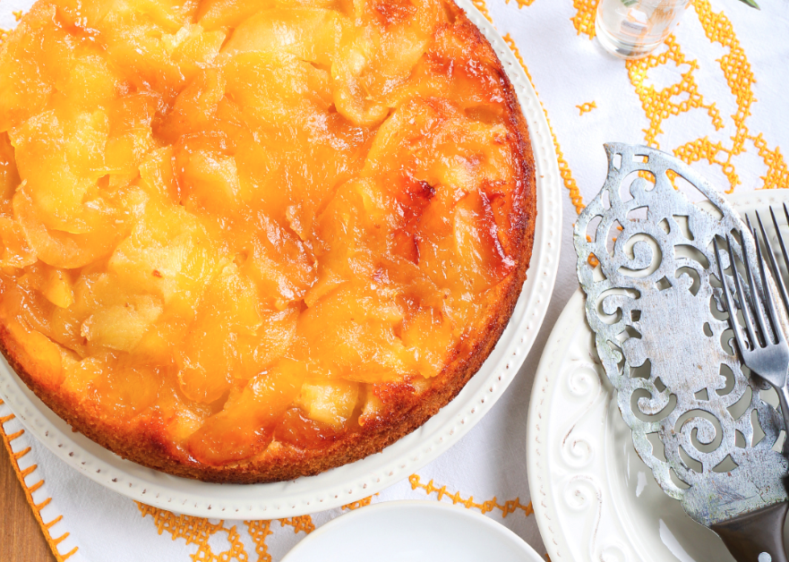 A gooey apple upside down cake on a white and orange towel with silver servingware.