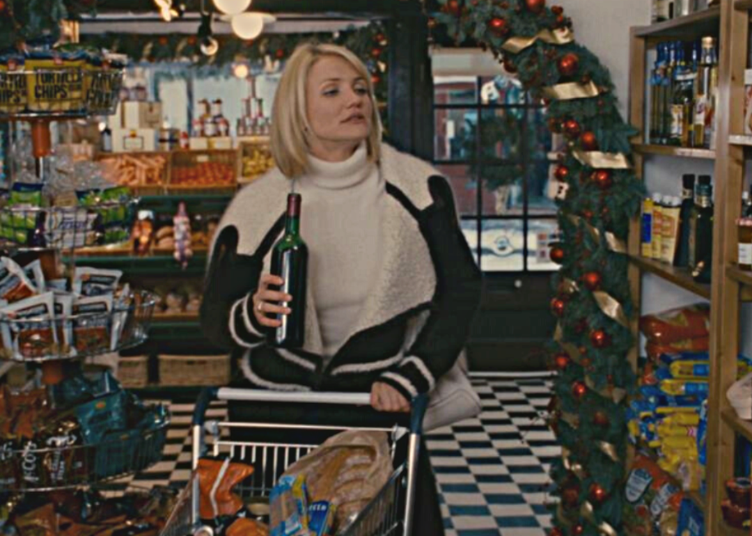 Cameron Diaz drinking from a bottle of wine while pushing a grocery cart at a small store.