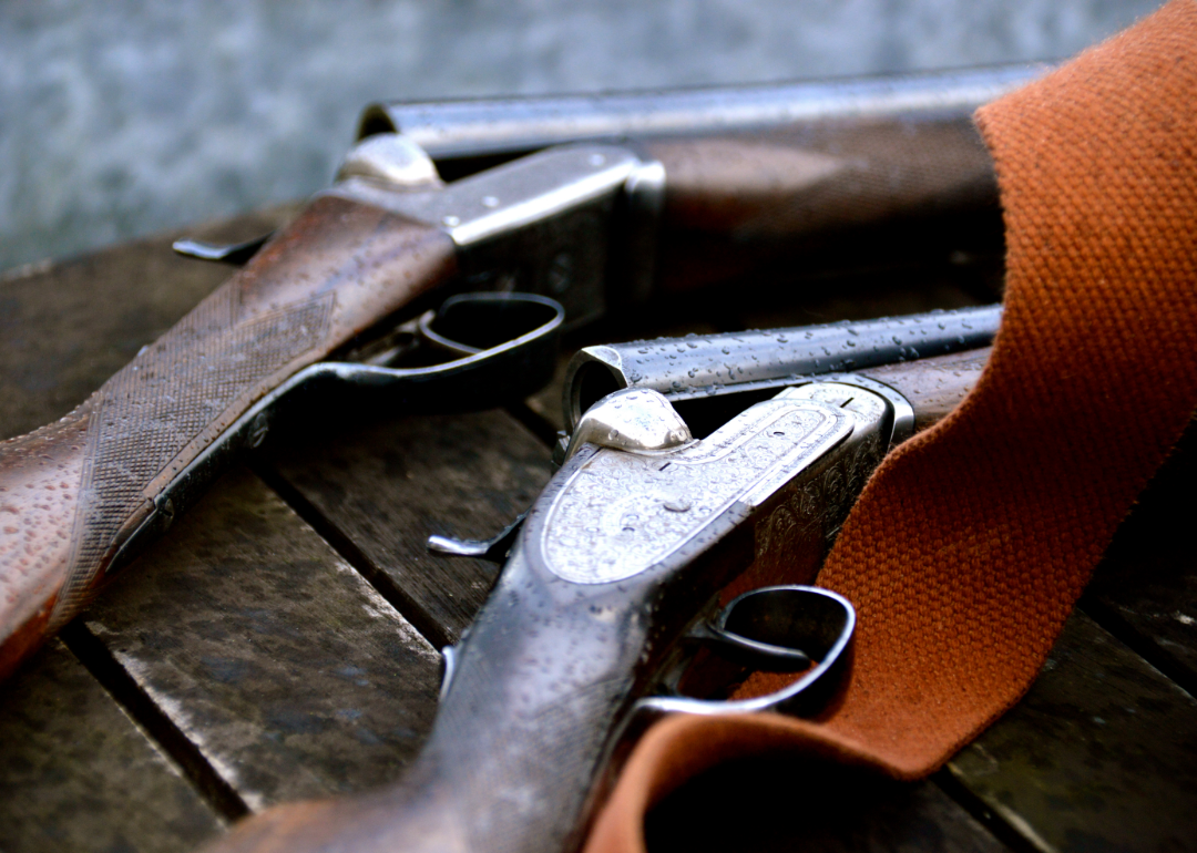 Two shotguns lying on a wooden surface.