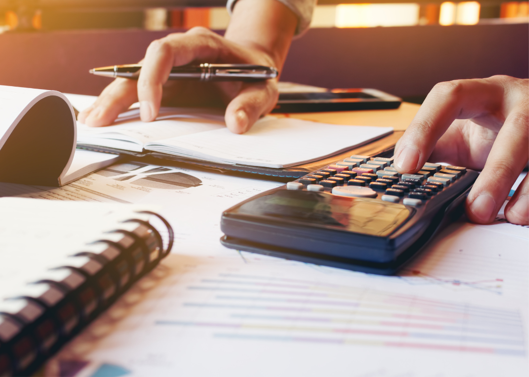 Two hands operating a calculator and taking notes in a notebook.