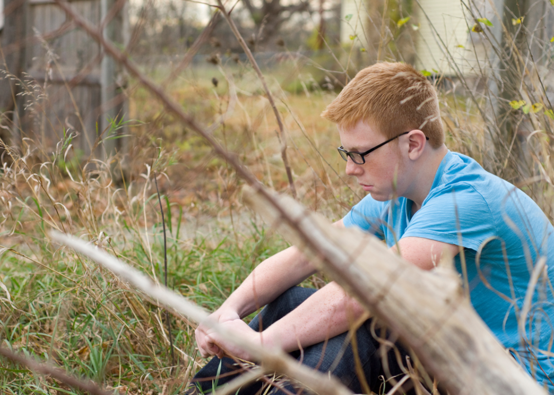 A teen sitting alone in a field with long grass.