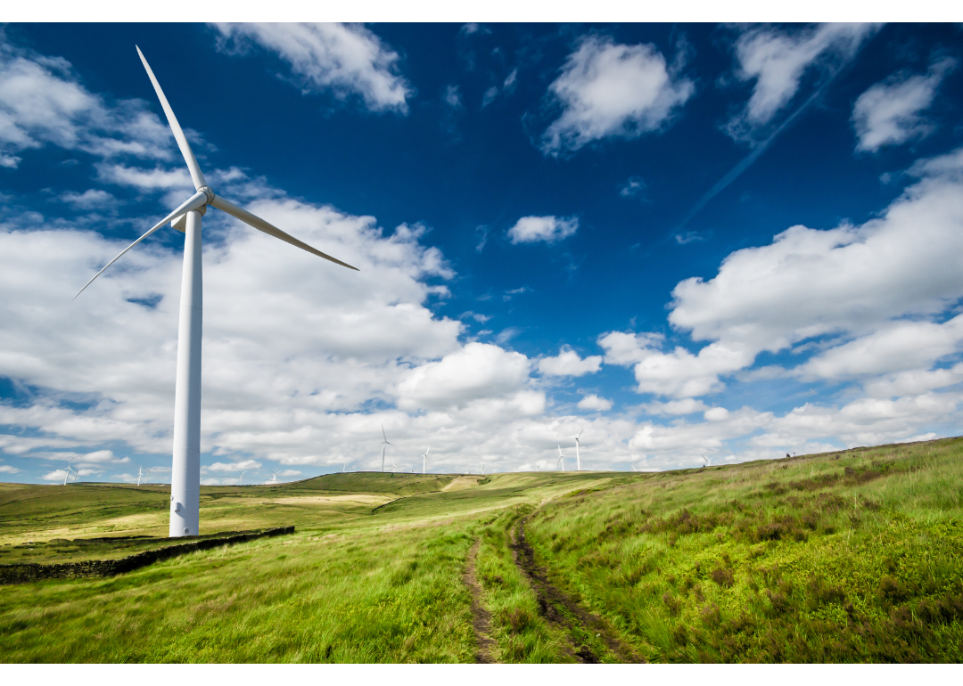 A white wind-powered turbine standing in a green field seen against a blue sky.