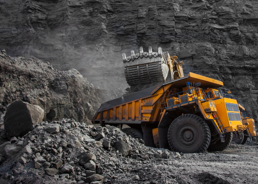 A heavy-duty truck digs into the ground at a coal mine site.