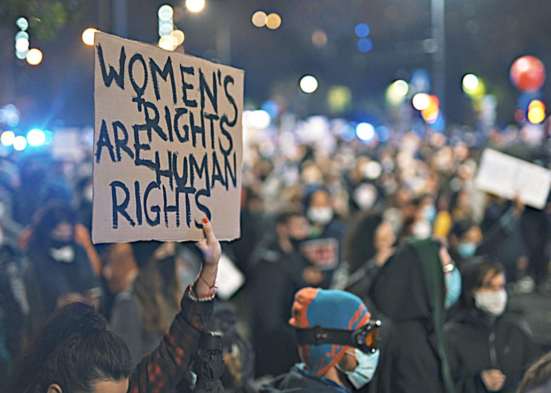 Image shows a rally of people with a person holding a sign that says "Women's rights are human rights" in the foreground
