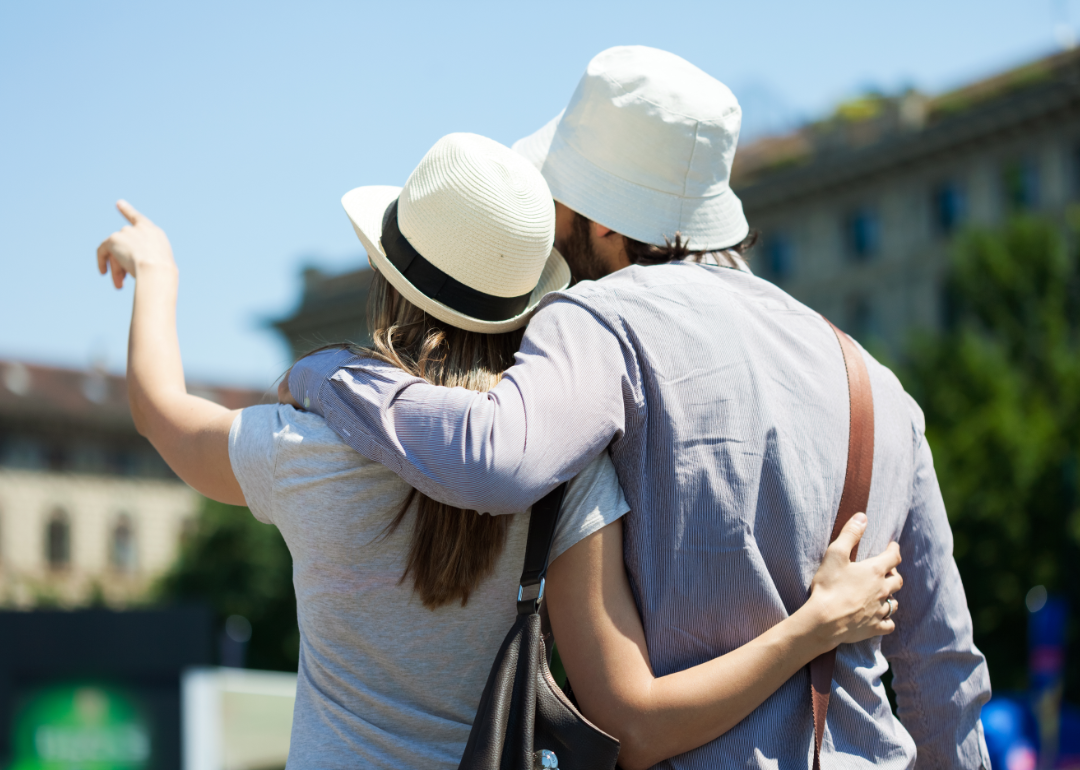 Rear view of a couple wearing white hats sightseeing and pointing into the distance.