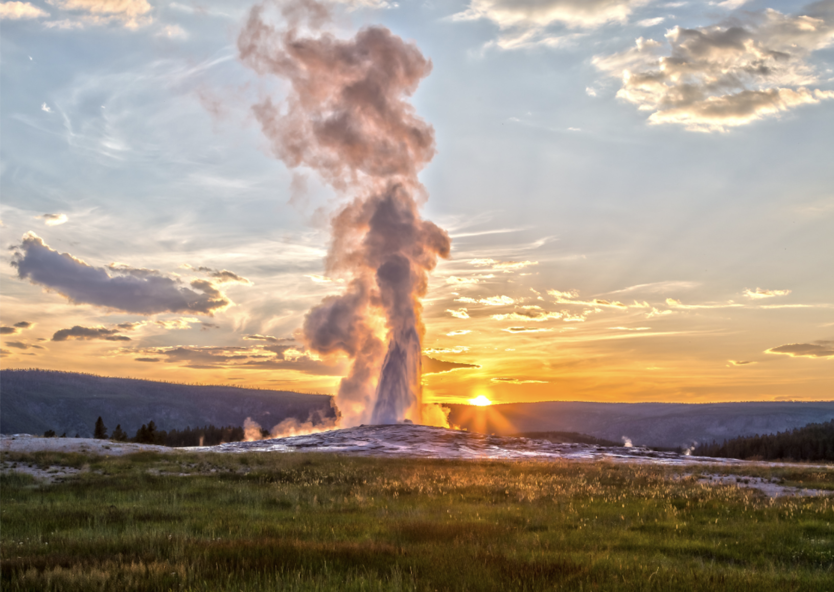 Old Faithful erupting in Yellowstone National Park at sunset.