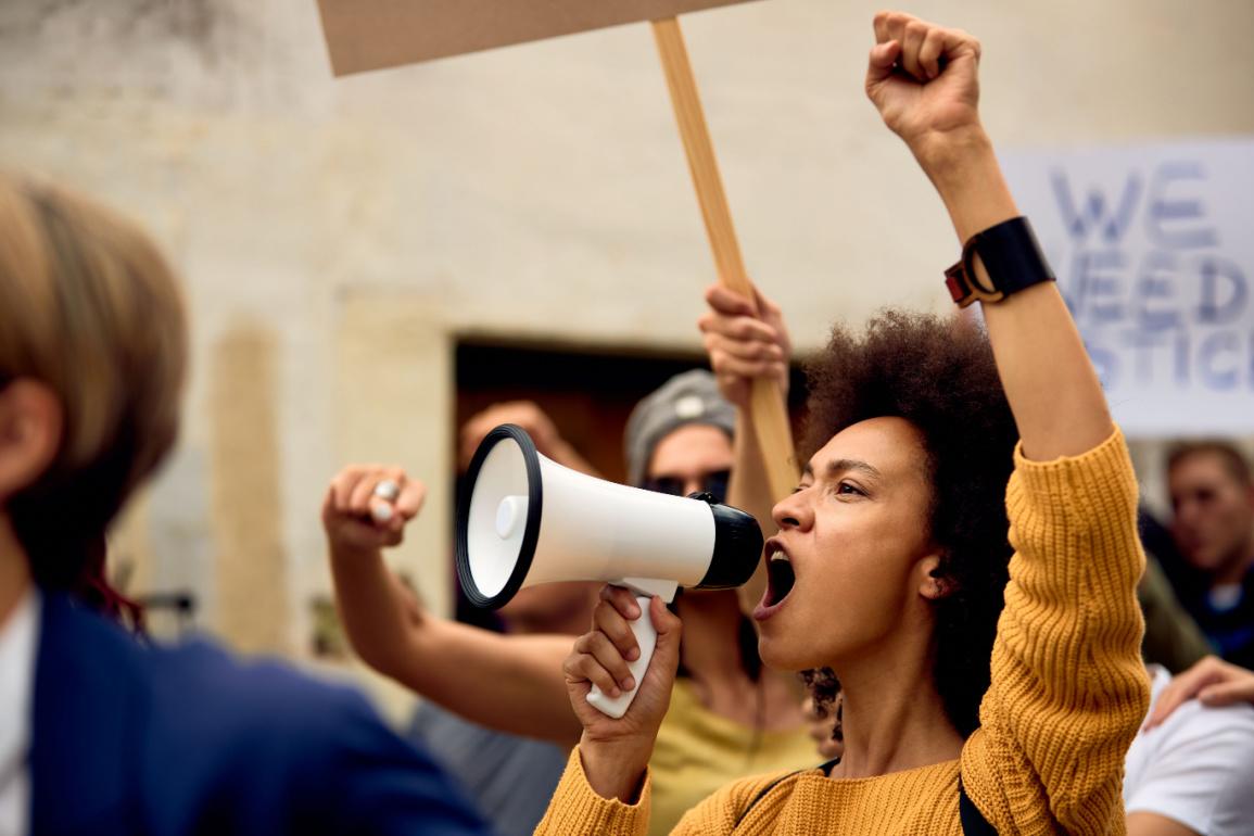 Image shows a women yelling through a megaphone at a women's rights rally