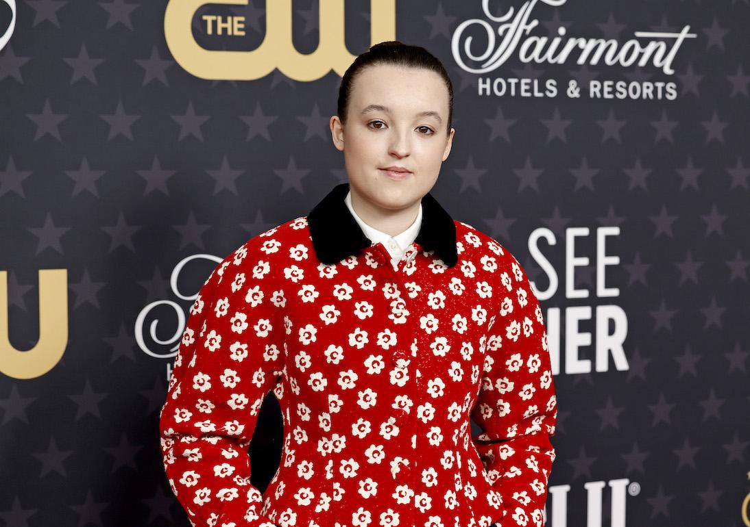Bella Ramsey attends red carpet event wearing a red, floral-printed jacket.