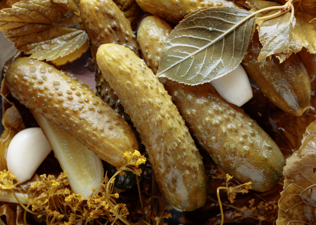 Brined pickles, sage, and garlic cloves on a table.