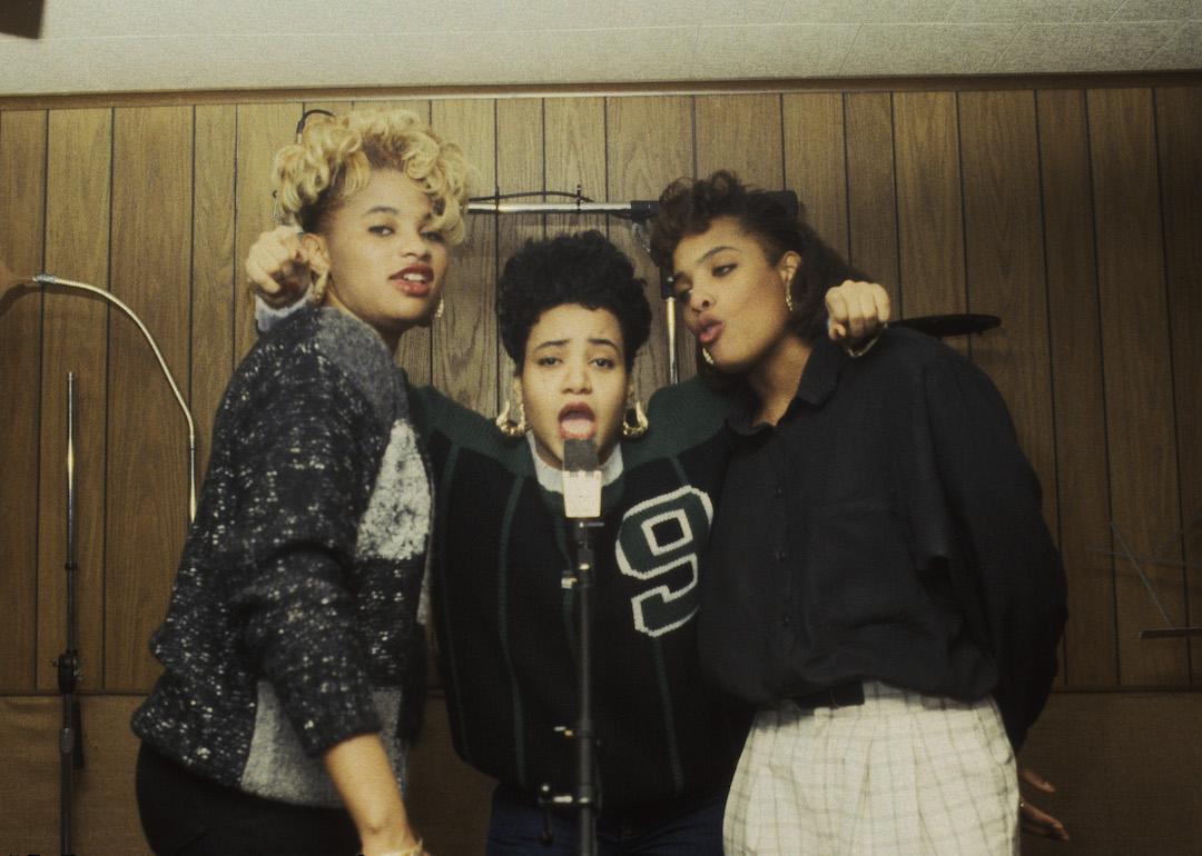 Salt (Cheryl James), Pepa (Sandra Denton), and DJ Spinderella (Deidra Roper) of Salt-N-Pepa posing in recording booth.