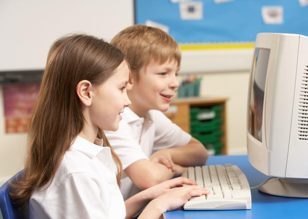 Elementary-aged students working on an old computer in their classroom.