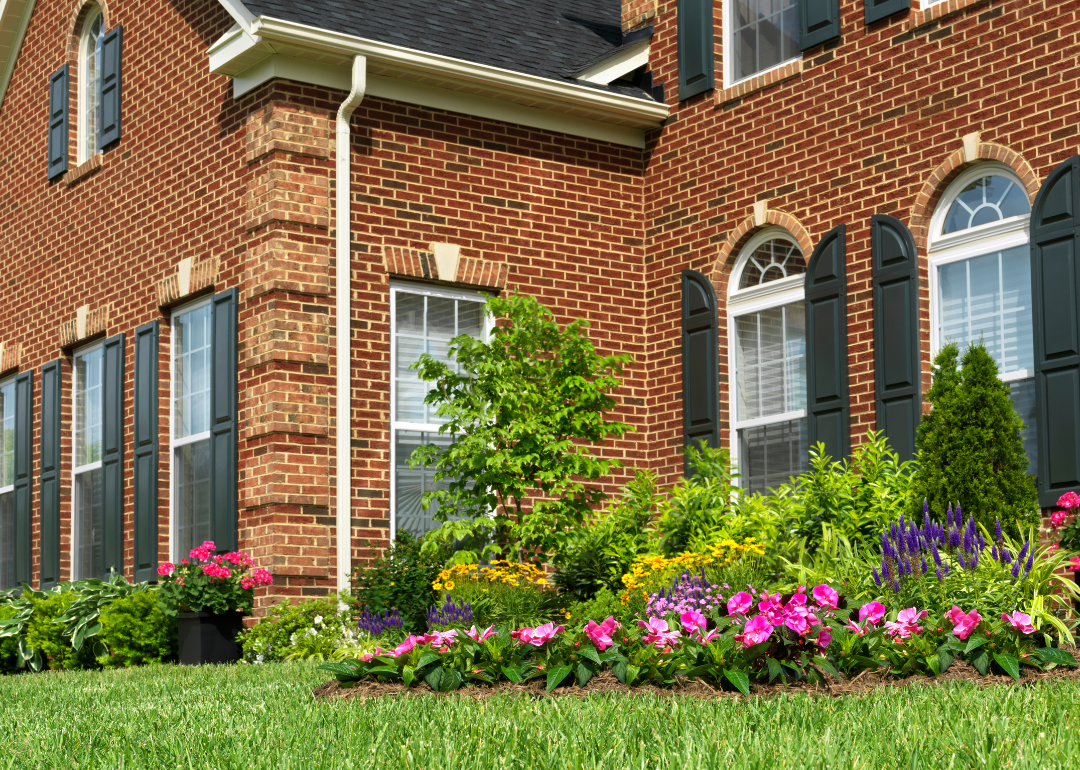 Exterior of a brick facade home with landscaping including a flower bed and lawn.