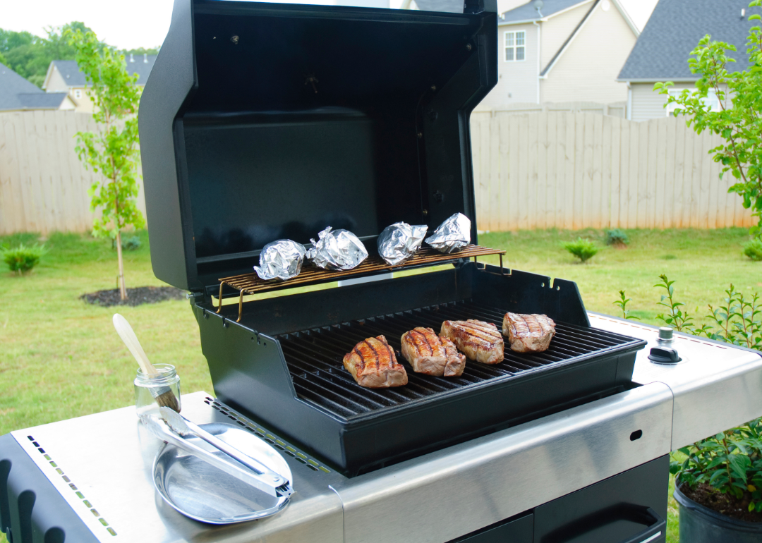 Meat and potatoes cooking on a gas grill.