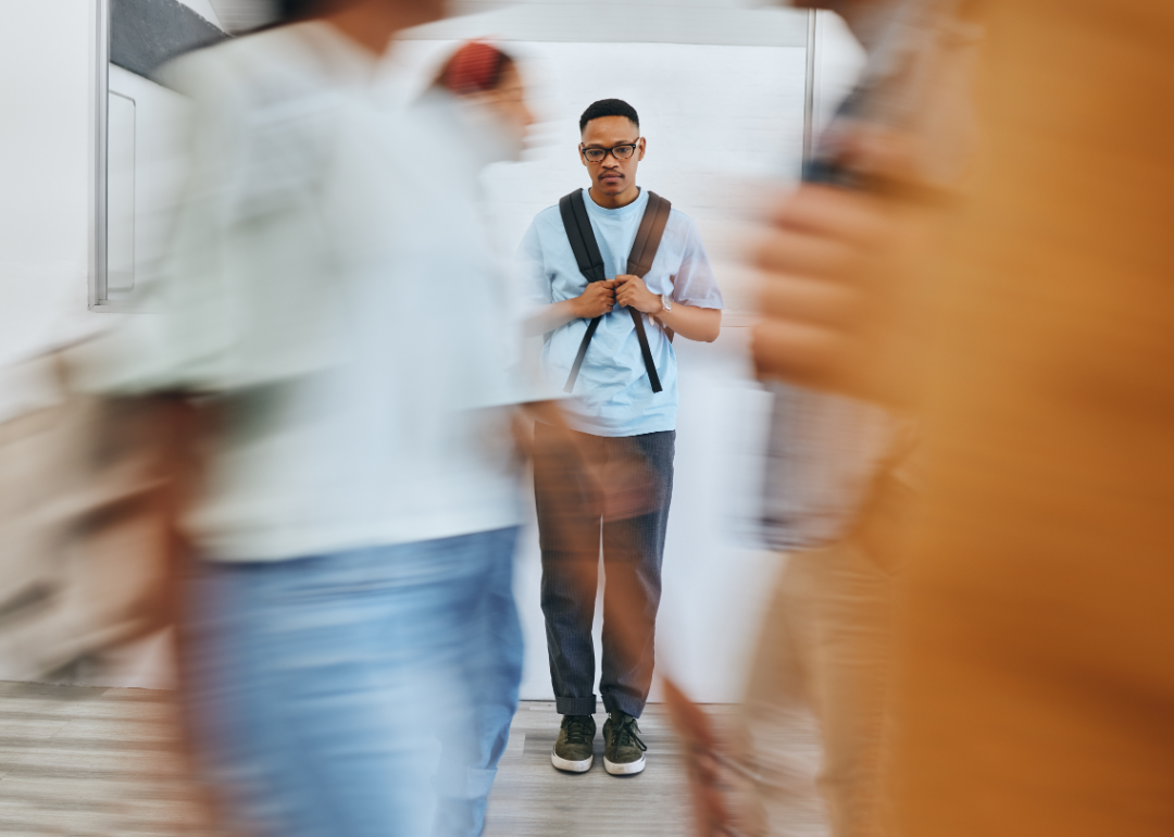 A young person stands still in a corridor and blurred images indicate others moving around them.