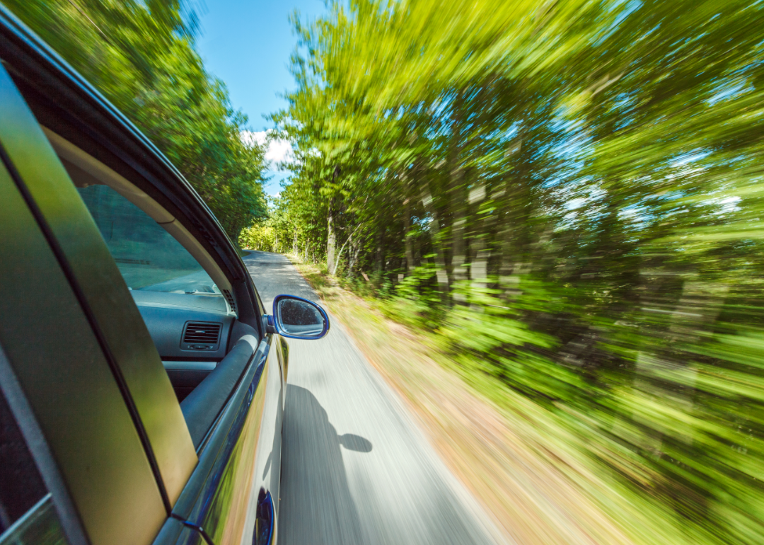 A car speeding along a country road in the summer.