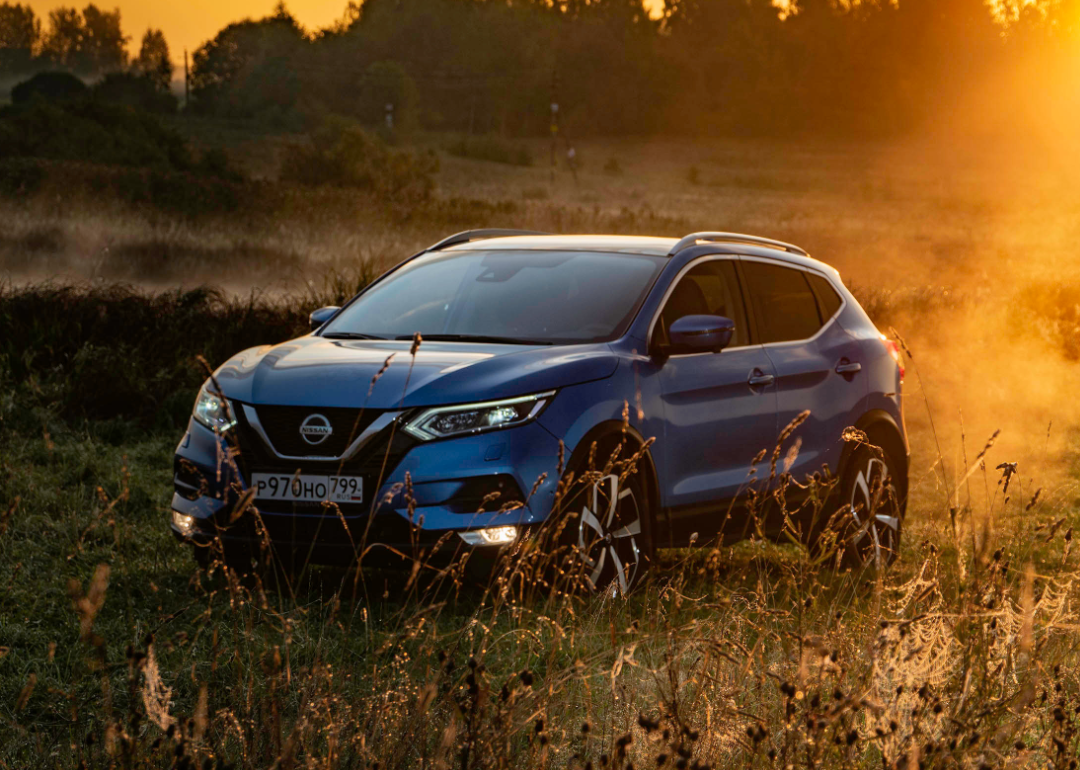 A blue Nissan SUV parked in a field at sunset.