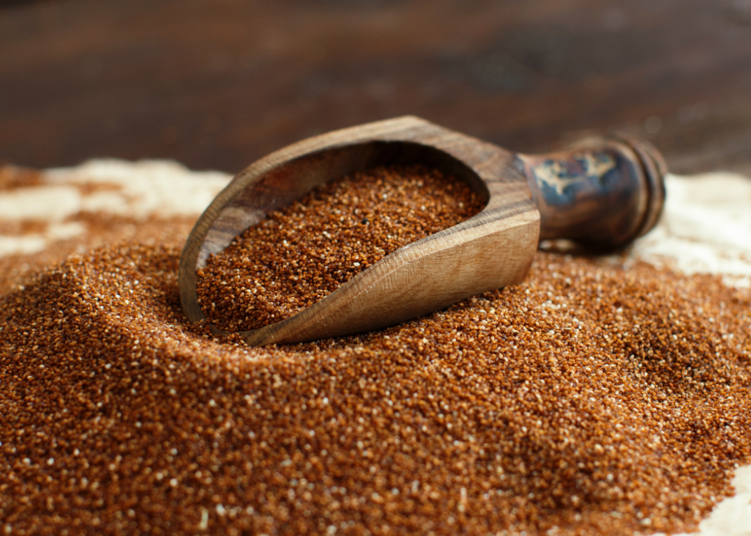 A pile of uncooked teff grain with a wooden scoop.