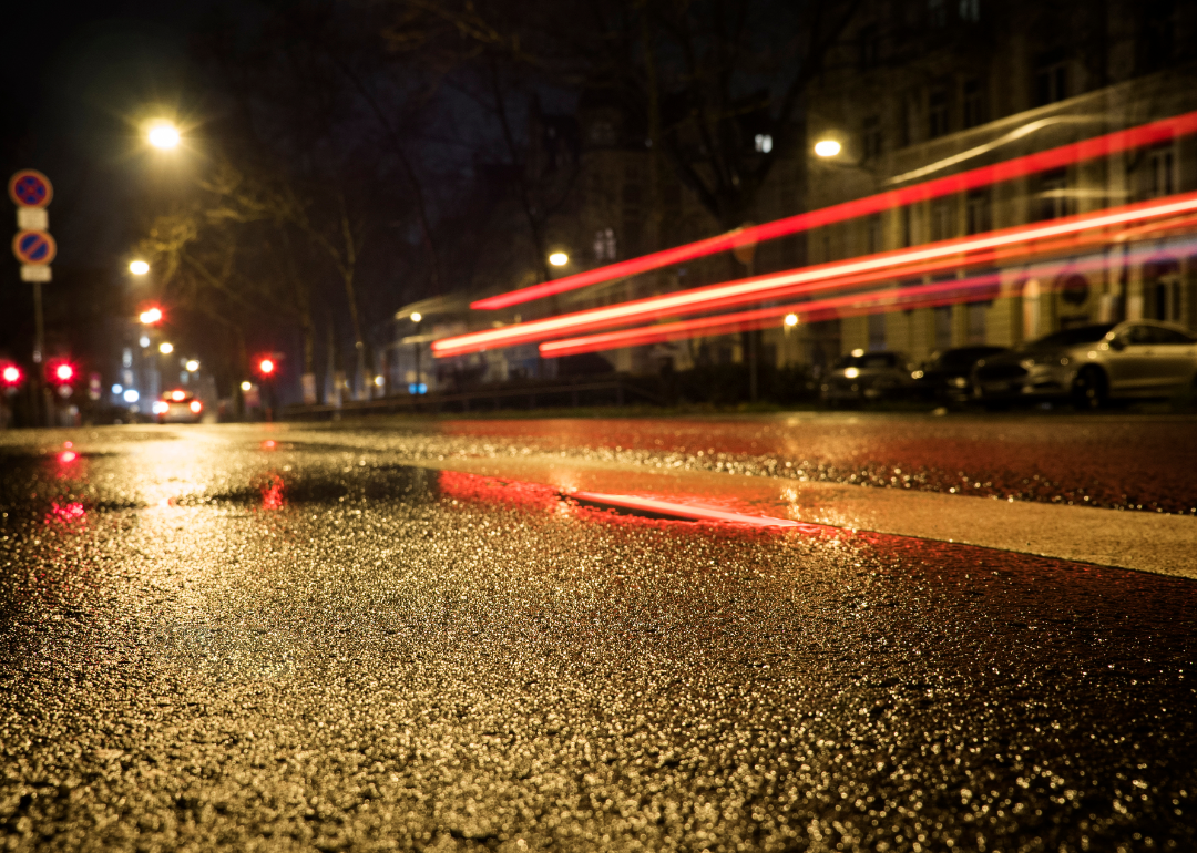 Tail lights of a car streaking across wet asphalt at night.