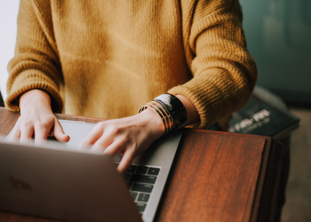 A person in a brown sweater works on a laptop.