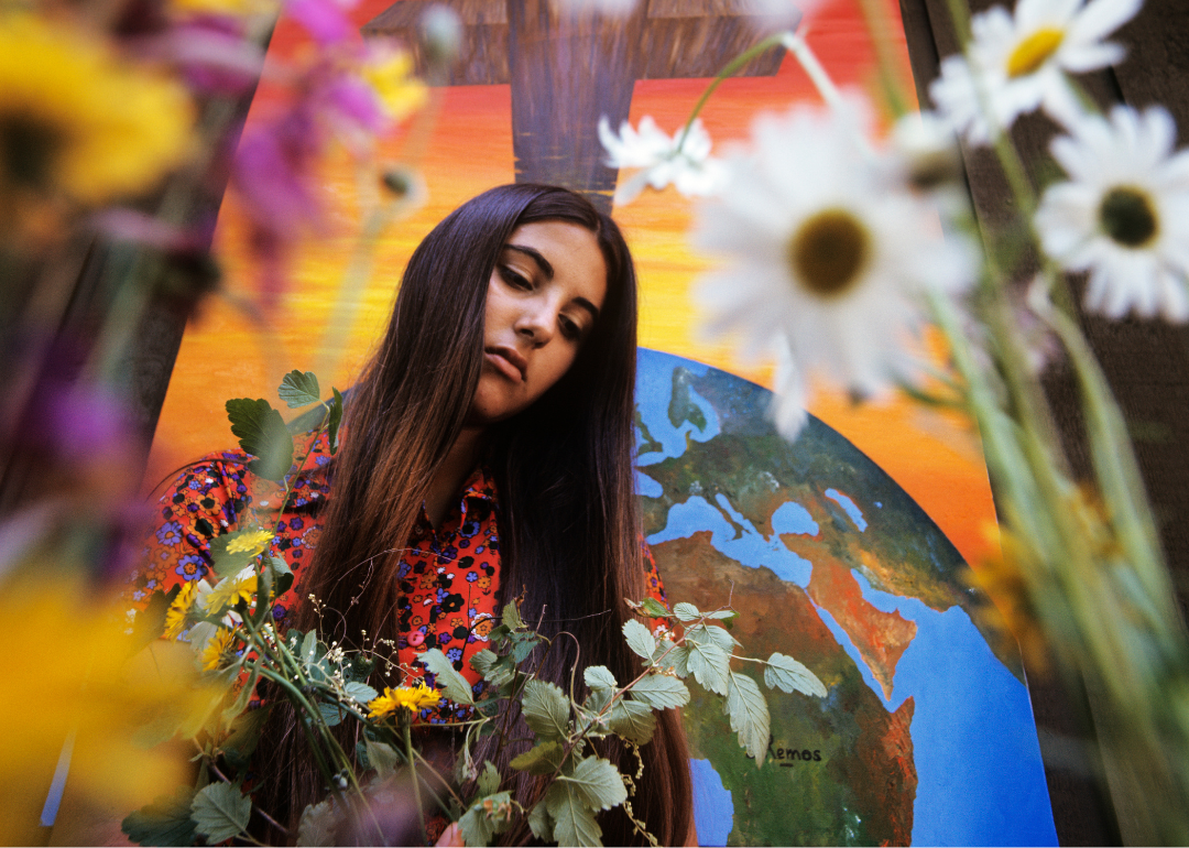 A woman in a colorful blouse sitting among daisies.