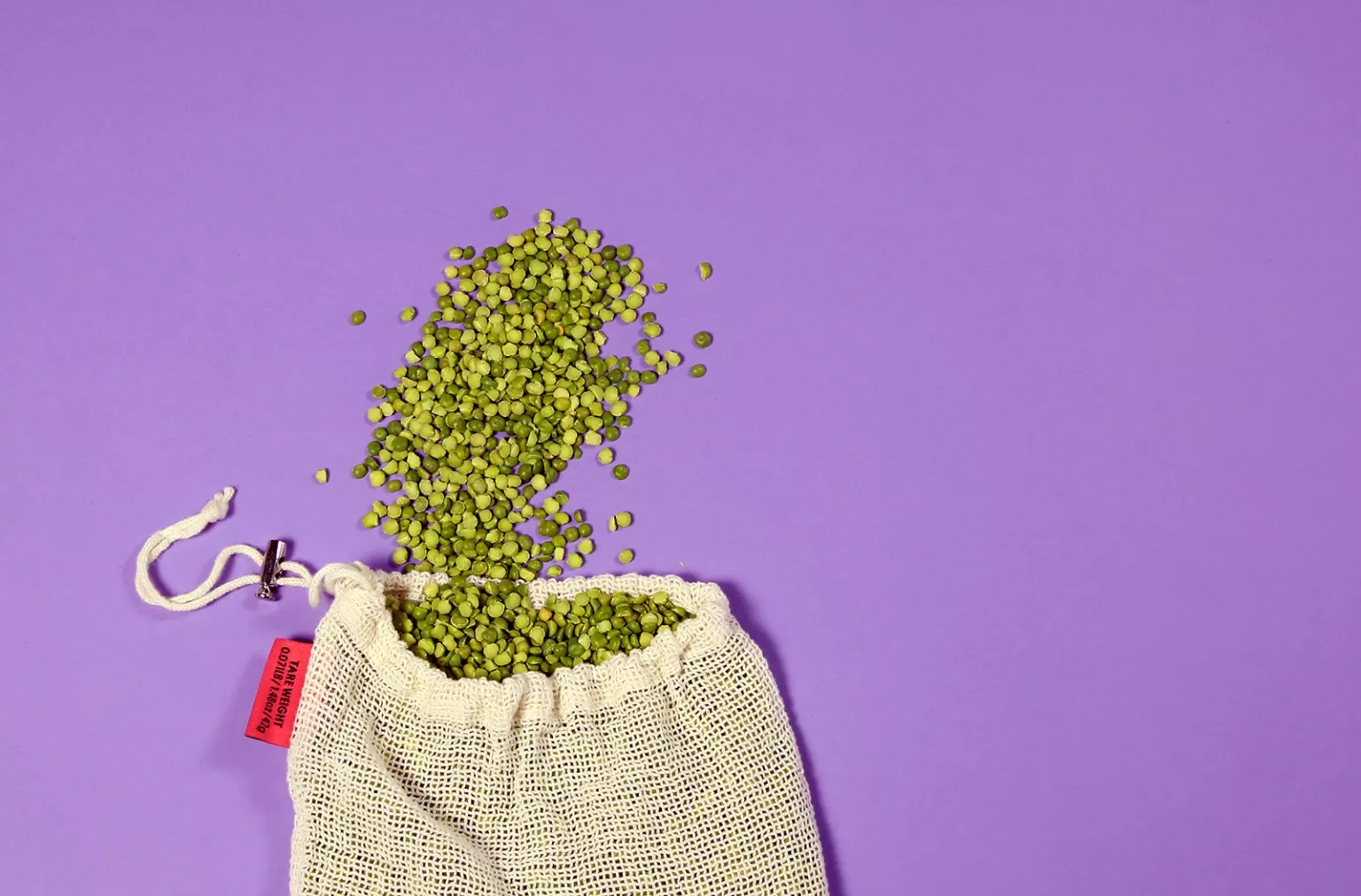 Split peas spill from the top of a fabric bag.