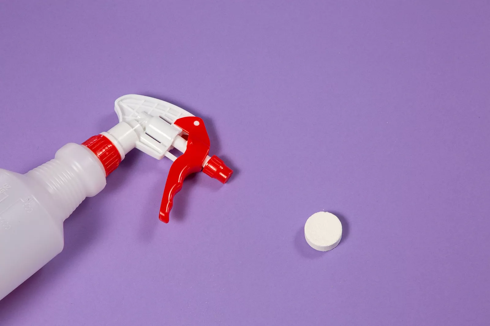 A plastic spray bottle sits next to a tablet of concentrated cleaning product.