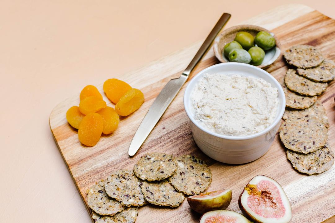 A vegan artisanal cheese on a cutting board with crackers, fruits and vegetables.