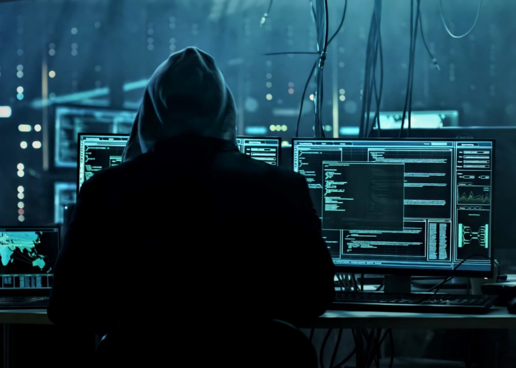 Hacker with computer screens in dark room.