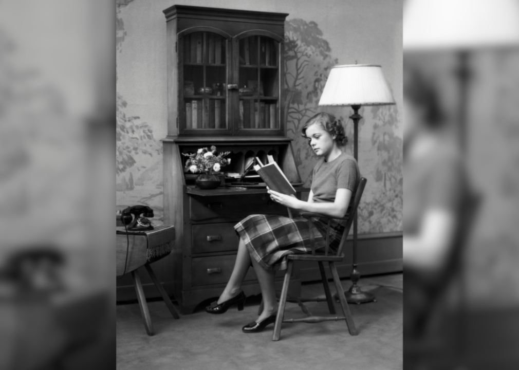 A woman sits beside a maple wood secretary desk.