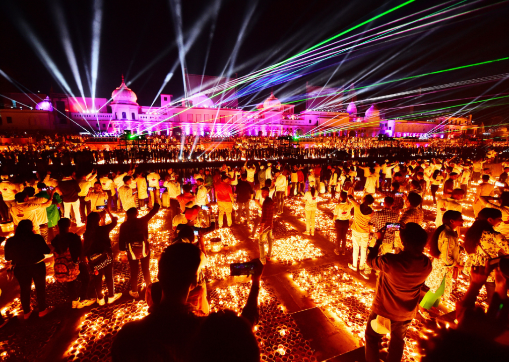 Crowds of people surrounded by lit candles in front of a palace that has strobe lights coming from it.