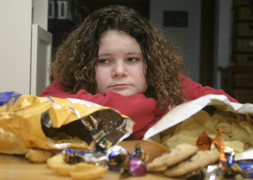 A sad looking child sits before an array of junk food.