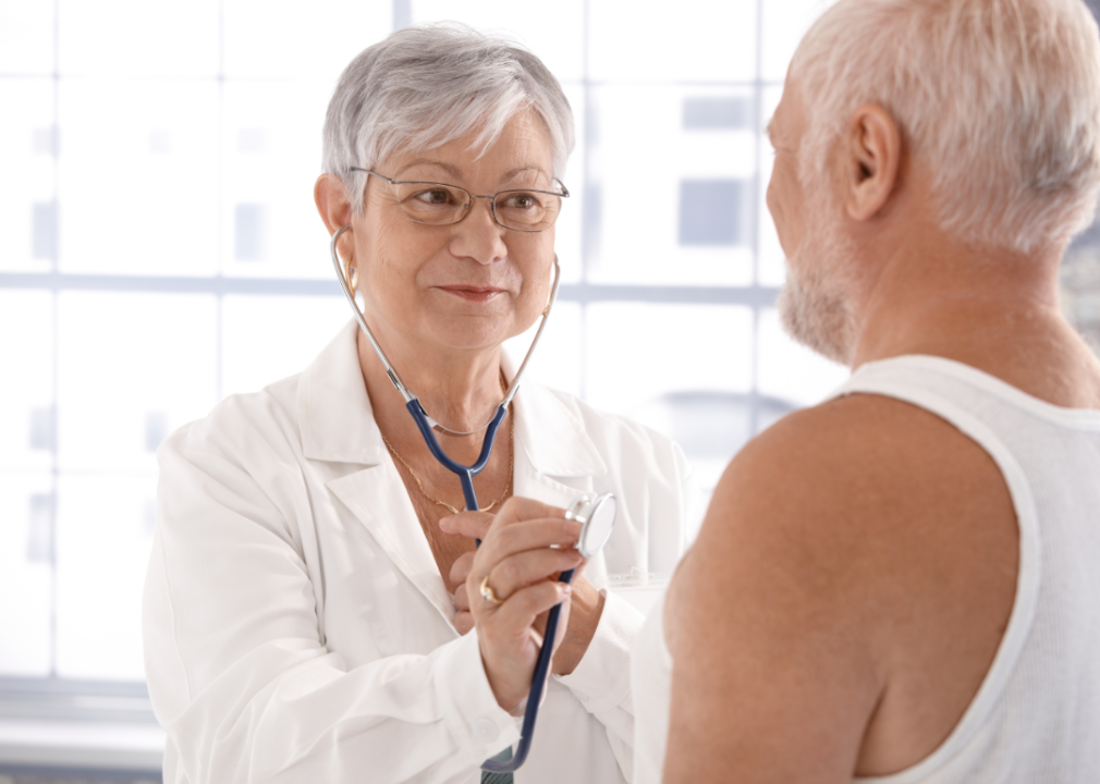 An older woman doctor examines an older man.