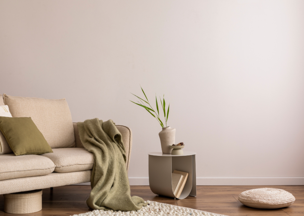 A beige walled room with a couch in a muted beige color with a green throw blanket on it