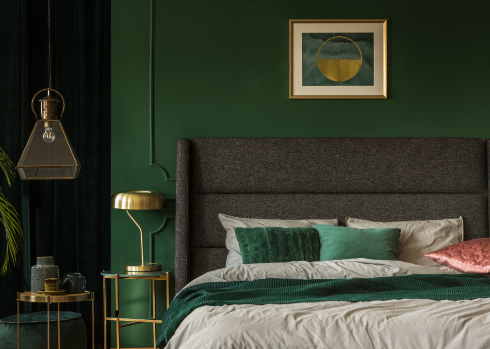 A bedroom with deeply green colored walls, a bed, and beige and green bedspread
