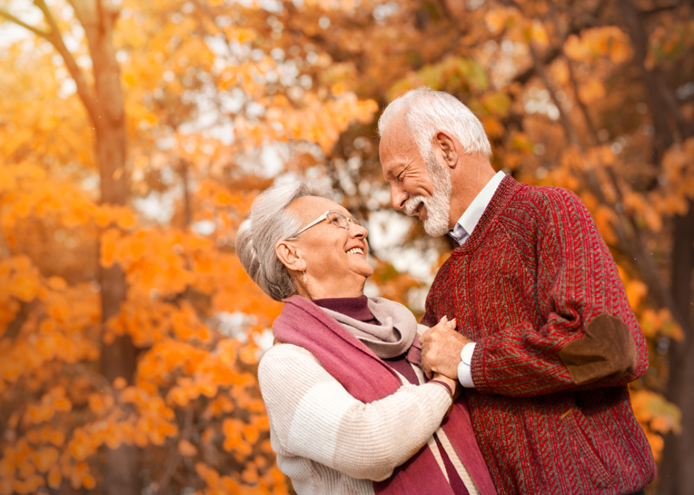 An older couple smile at one another with a fall background