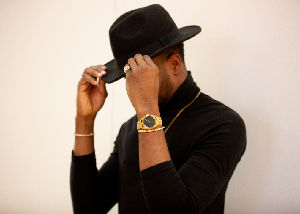 Stylish Black man wearing black fedora while flexing jewelry.
