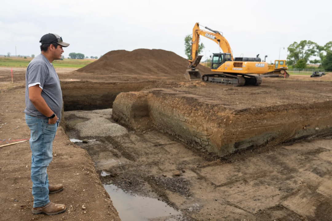 Joey Goodthunder looks at a foundation being dug with heavy machinery