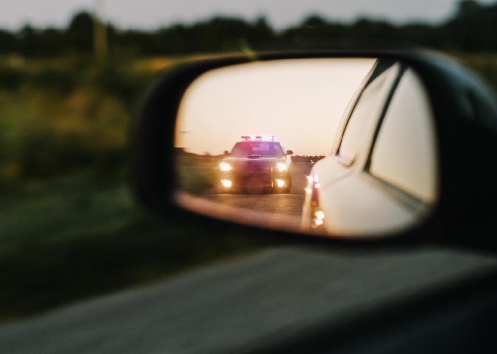 Police give more speeding tickets to Black, Hispanic, and AAPI rideshare drivers than white ones, data shows car sideview mirror of police lights approaching