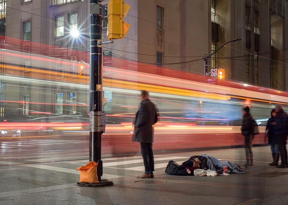 unhoused person sleeps on the streets in Toronto with motion blur of traffic driving by