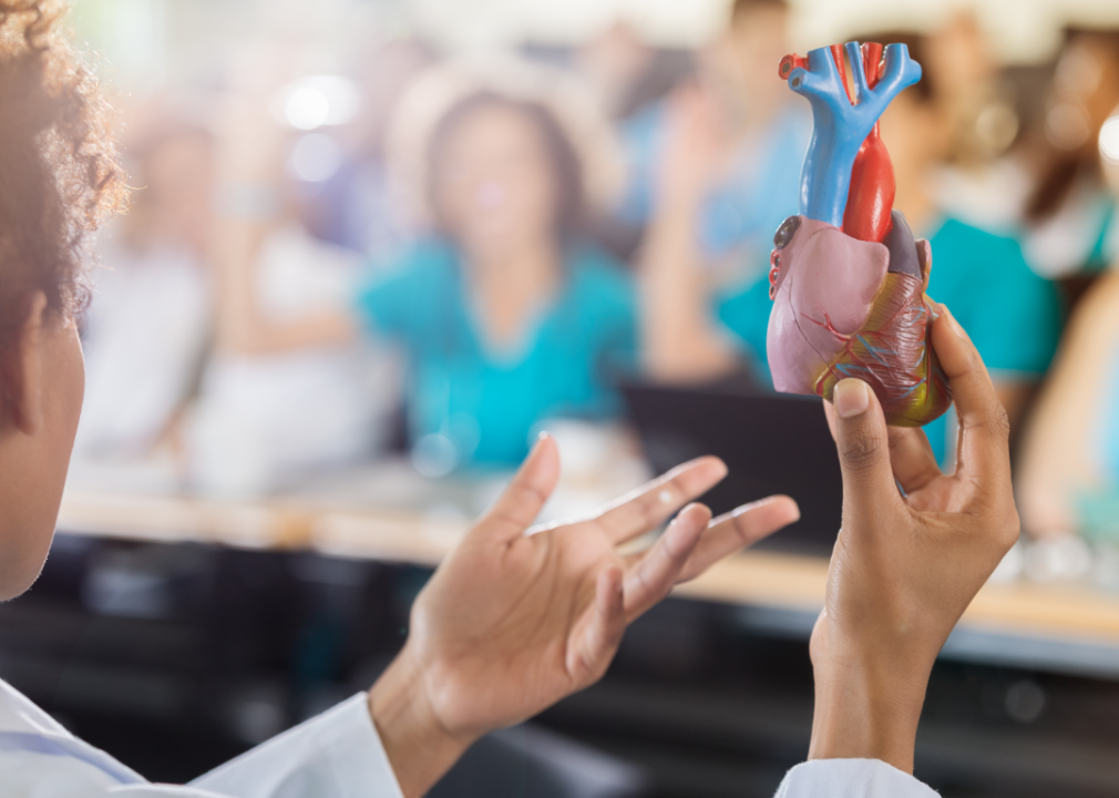 woman holding up model of human heart in front of classroom 